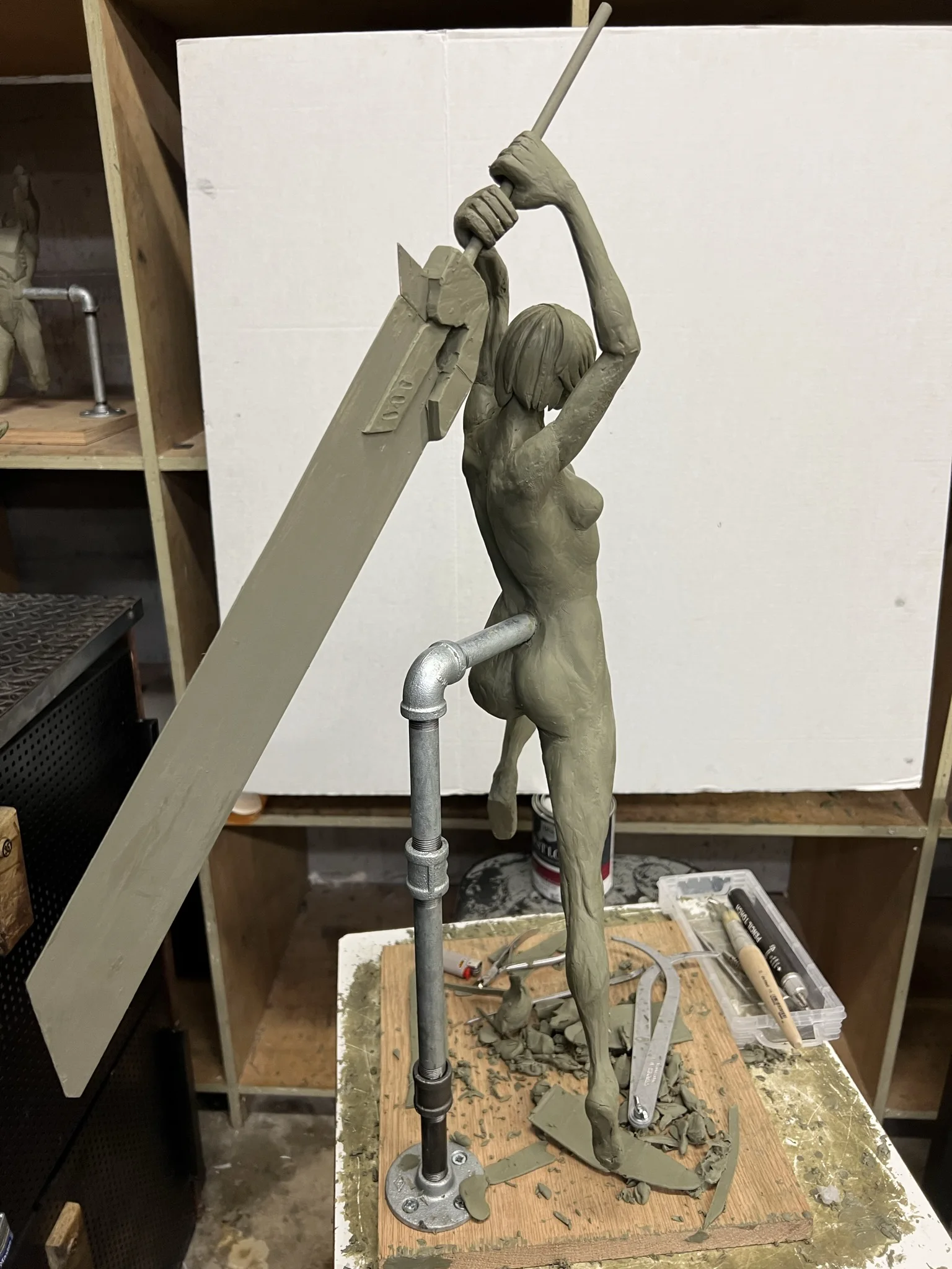 Clay figure leaping on a pipe armature, holding a large sword overhead.